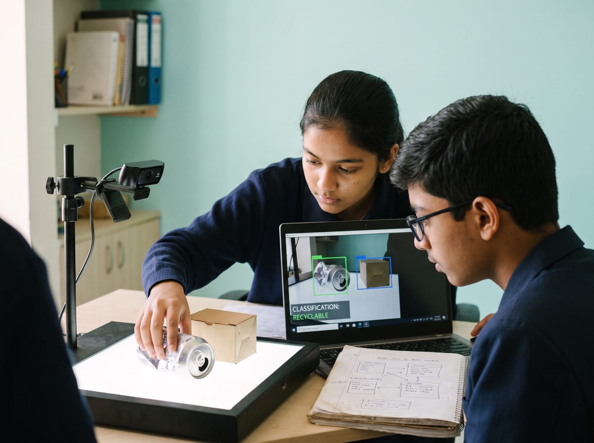 Two students testing an image classifier on a laptop as it labels a can as recyclable